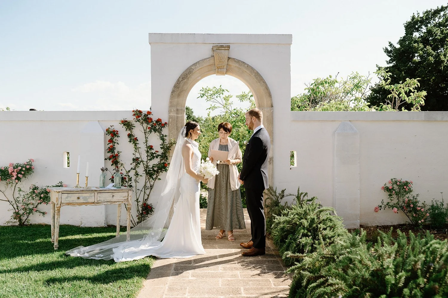 A ceremony under a stone arch dressed with flowers in the garden of the masseria