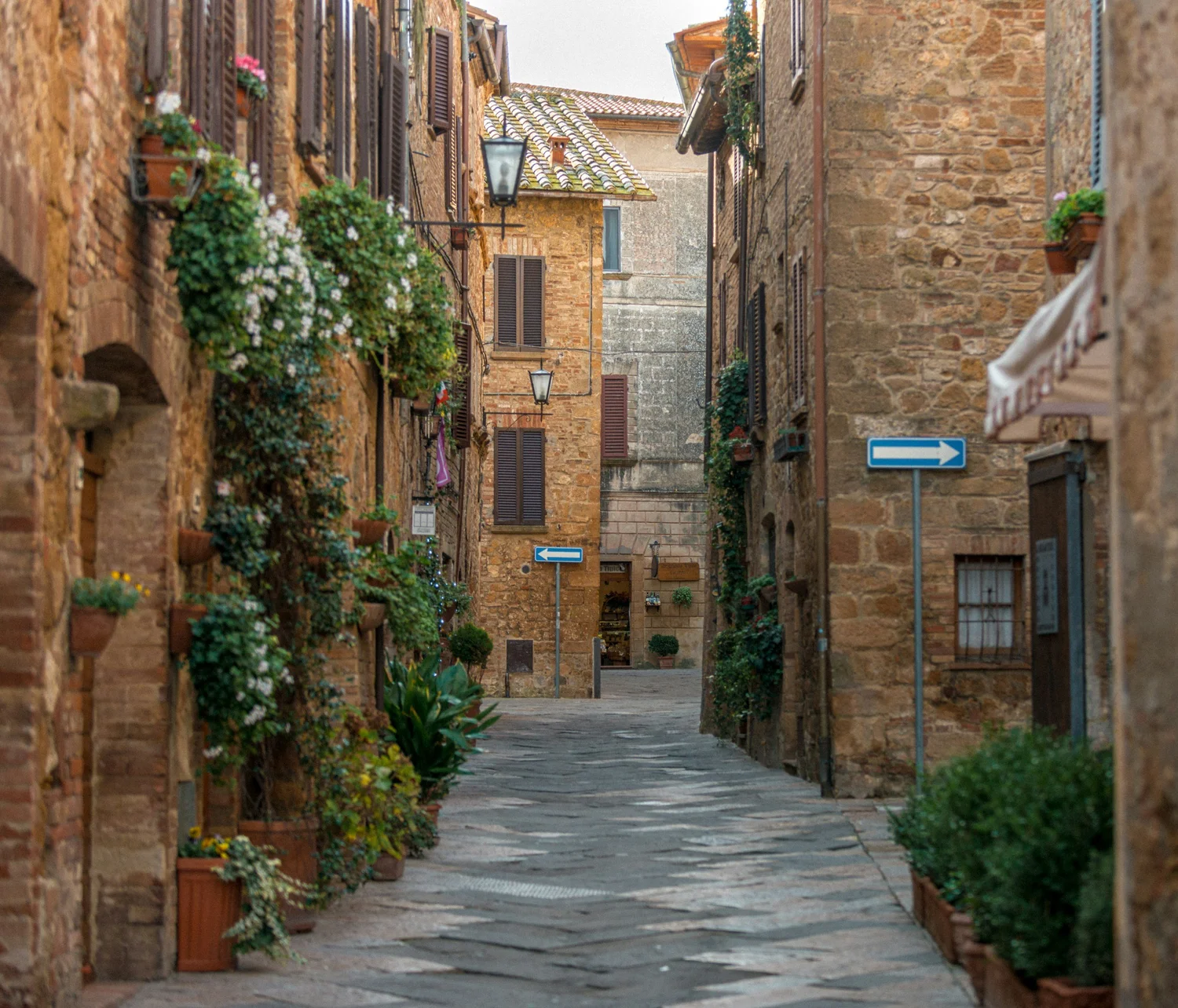 A narrow European street with old brick buildings, flower boxes, and shutters, and a street sign with an arrow pointing right.