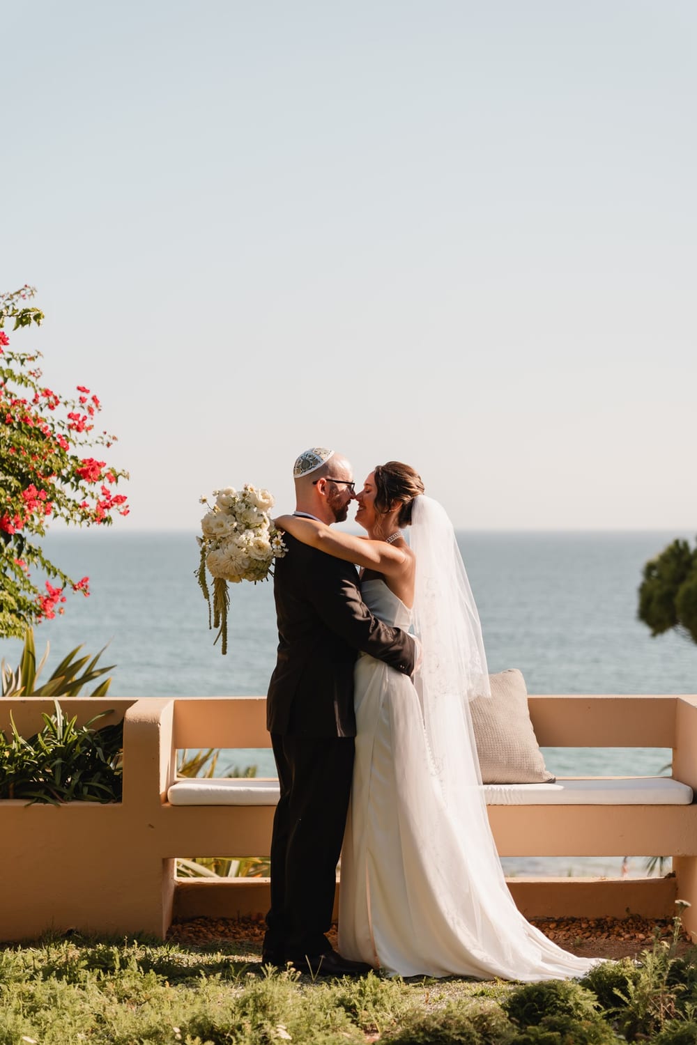 A couple embracing on a seaside terrace with flowers and the sea behind them