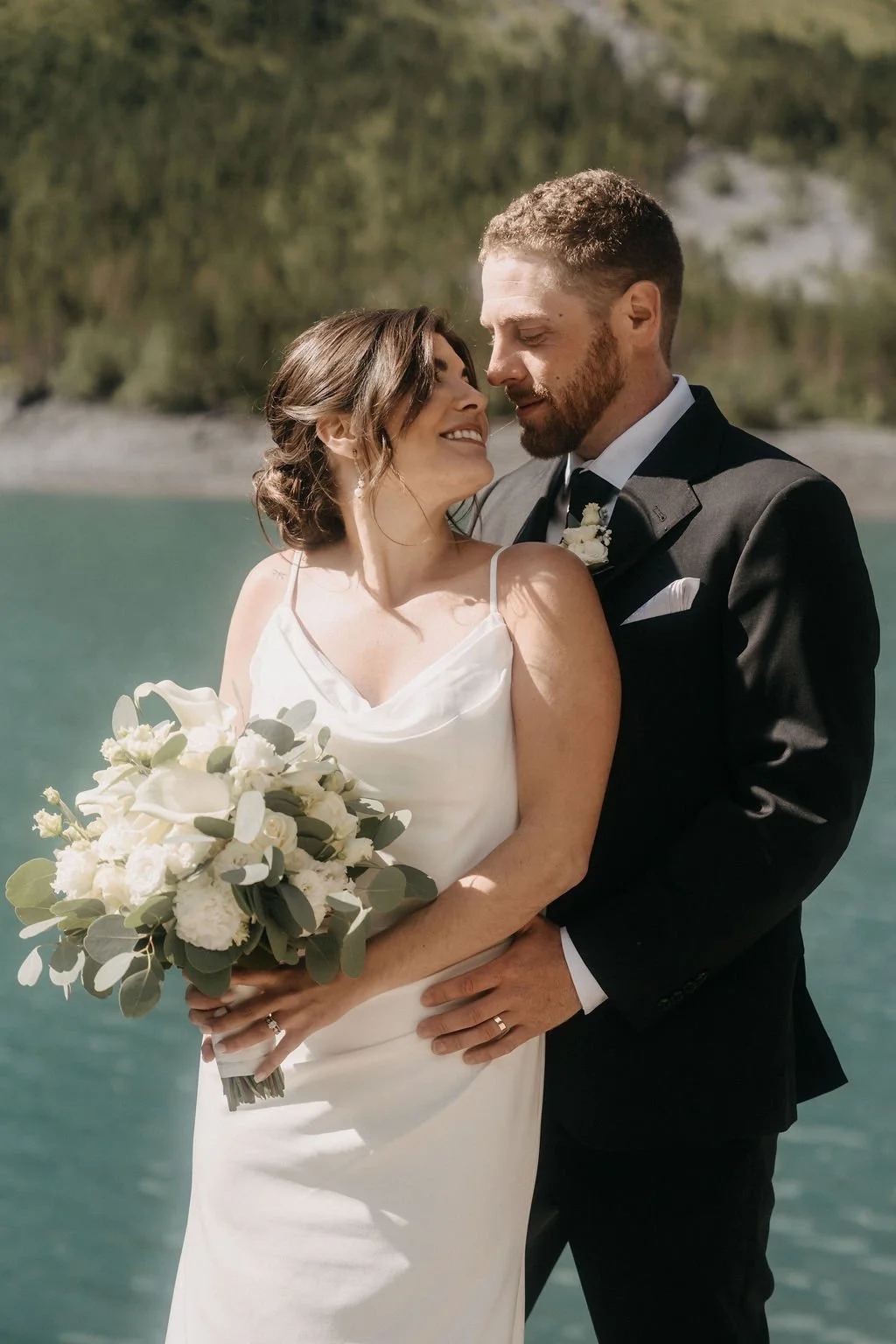 A bride and groom smiling by an alpine lake, Switzerland elopement